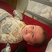 Finley joined the competition — help win amazing prizes! baby, infant, smiling, swaddle, blanket, pacifier, bottle, bed, playpen, soft_toys, clothing, face, person, indoors, baby_bedding, cute, child, sleepwear, resting, comfort