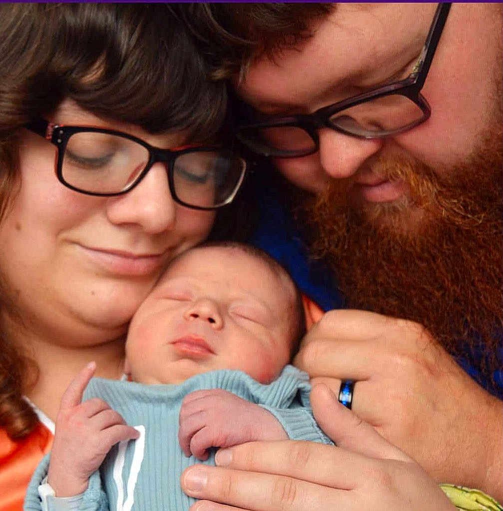 Timothy is registered to the contest to win money with this photo: baby, newborn, sleeping, couple, glasses, beard, woman, man, love, family, hands, closeup, portrait, tenderness, affection, indoor, clothing, human, skin, head