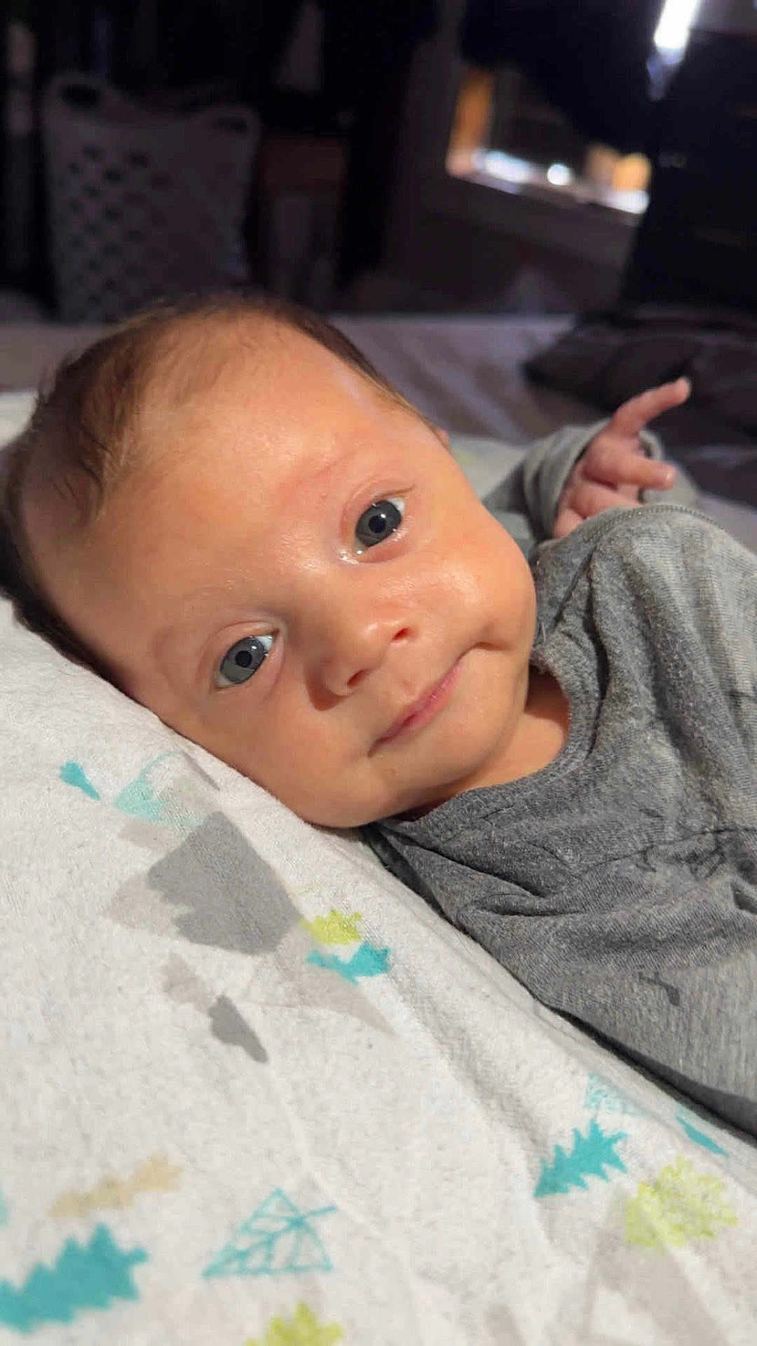 Levi is registered to the contest to win money with this photo: baby, infant, face, eyes, smile, blanket, pattern, gray_clothing, lying_down, indoor, child, skin, person, head, cute, young, portrait, cozy, soft_light, expression