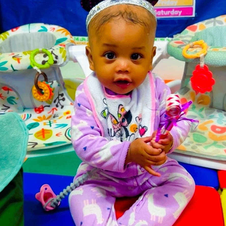 Layla Gilmore is registered to the contest to win money with this photo: baby, child, pajamas, purple, play_mat, toys, headband, new_year, classroom, educational_posters, colorful, sitting, infant, celebration, holding, smiling, indoor, cute, festive, play_area