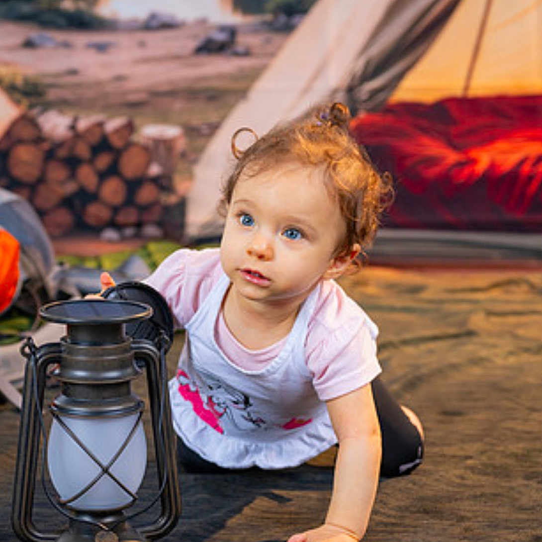 Viviana is registered to the contest to win money with this photo: adventure, blue_eyes, camping, casual_clothing, child, crawling, curly_hair, cute, daylight, explorer, firewood, ground, lantern, nature, outdoor, playful, portrait, soft_lighting, tent, toddler