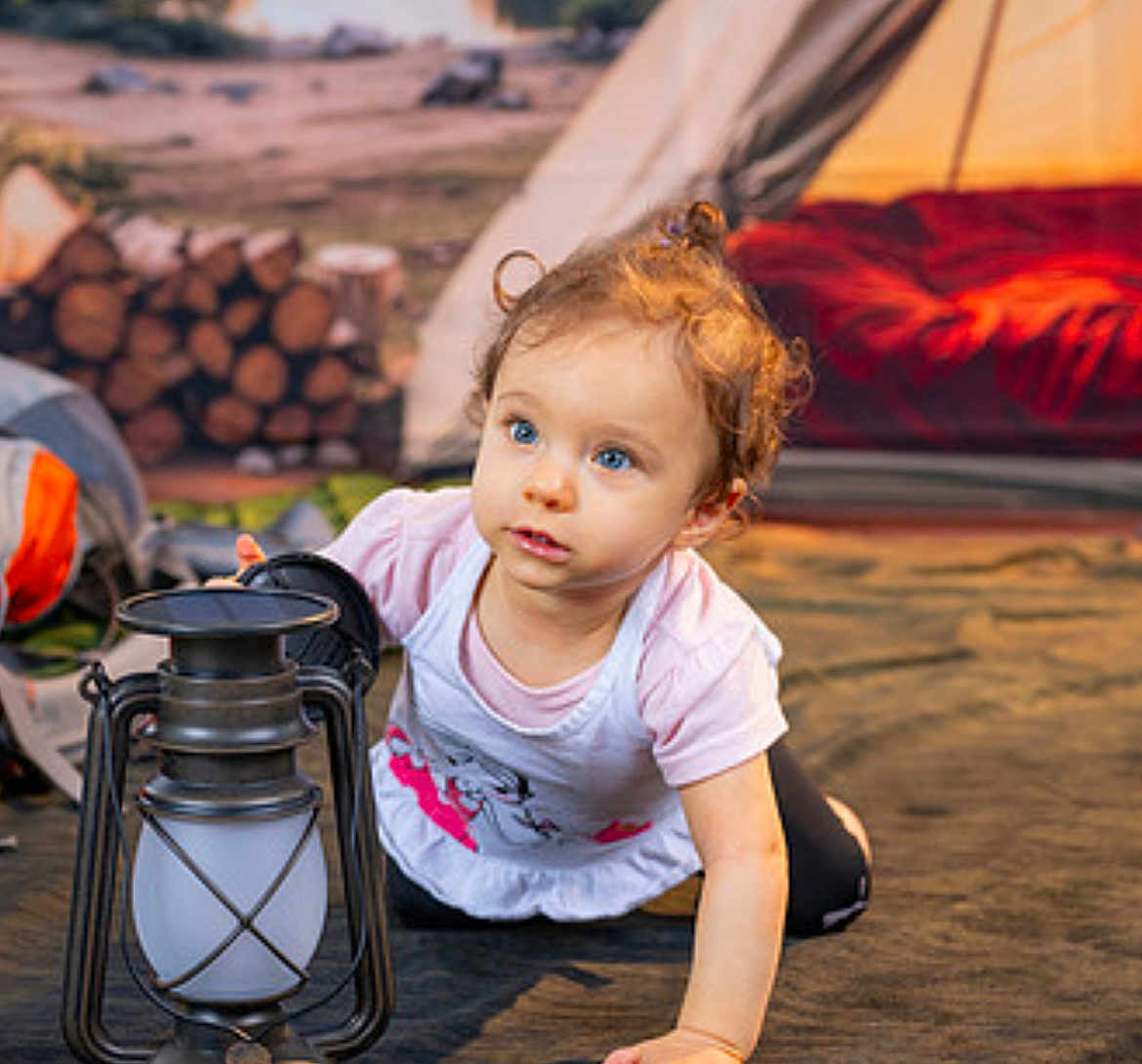 Viviana is registered to the contest to win money with this photo: toddler, child, lantern, camping, tent, firewood, outdoor, curly_hair, blue_eyes, crawling, adventure, nature, explorer, casual_clothing, soft_lighting, ground, playful, daylight, portrait, cute