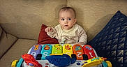 Jade participe au concours pour gagner de l'argent avec cette photo : animal_illustrations, baby, child, clothing, colorful, couch, curious, cushion, expression, face, furniture, hands, home, indoor, infant, numbers, piano, play, seated, toy