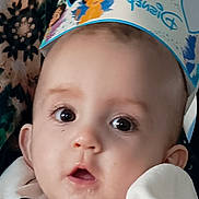 Jade participe au concours pour gagner de l'argent avec cette photo : baby, child, close_up, crown, curious, cute, disney, expression, face, hand, headwear, holding, indoor, infant, patterned_background, portrait, soft_lighting, white_clothing, wide_eyes, young_child