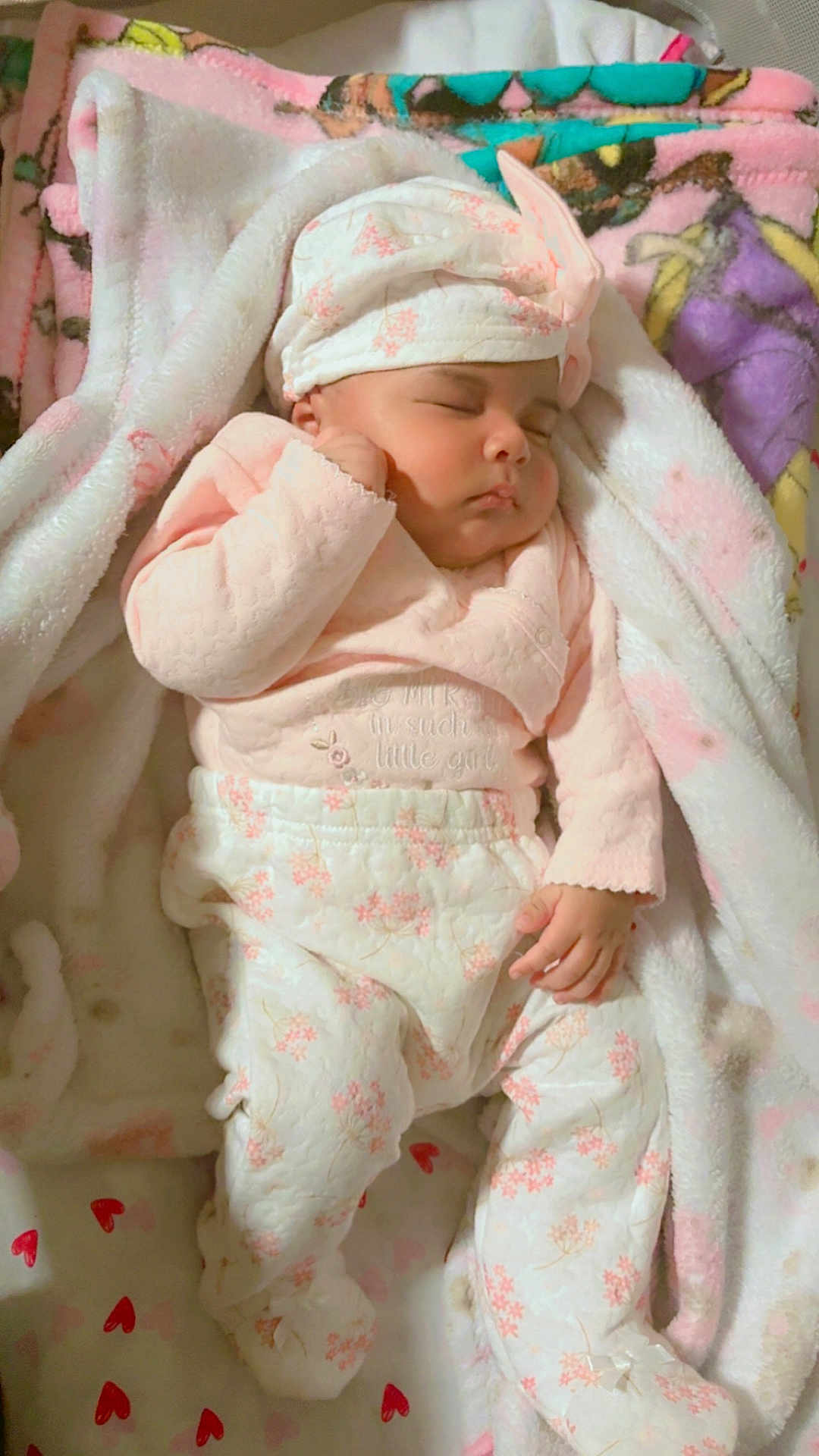 Sandra Gonzalez joined the competition — help win amazing prizes! baby, sleeping, blanket, pink_clothing, white_clothing, hat, infant, cozy, floral_pattern, soft_texture, cute, peaceful, indoor, child, newborn, resting, person, footed_pajamas, headwear, closeup