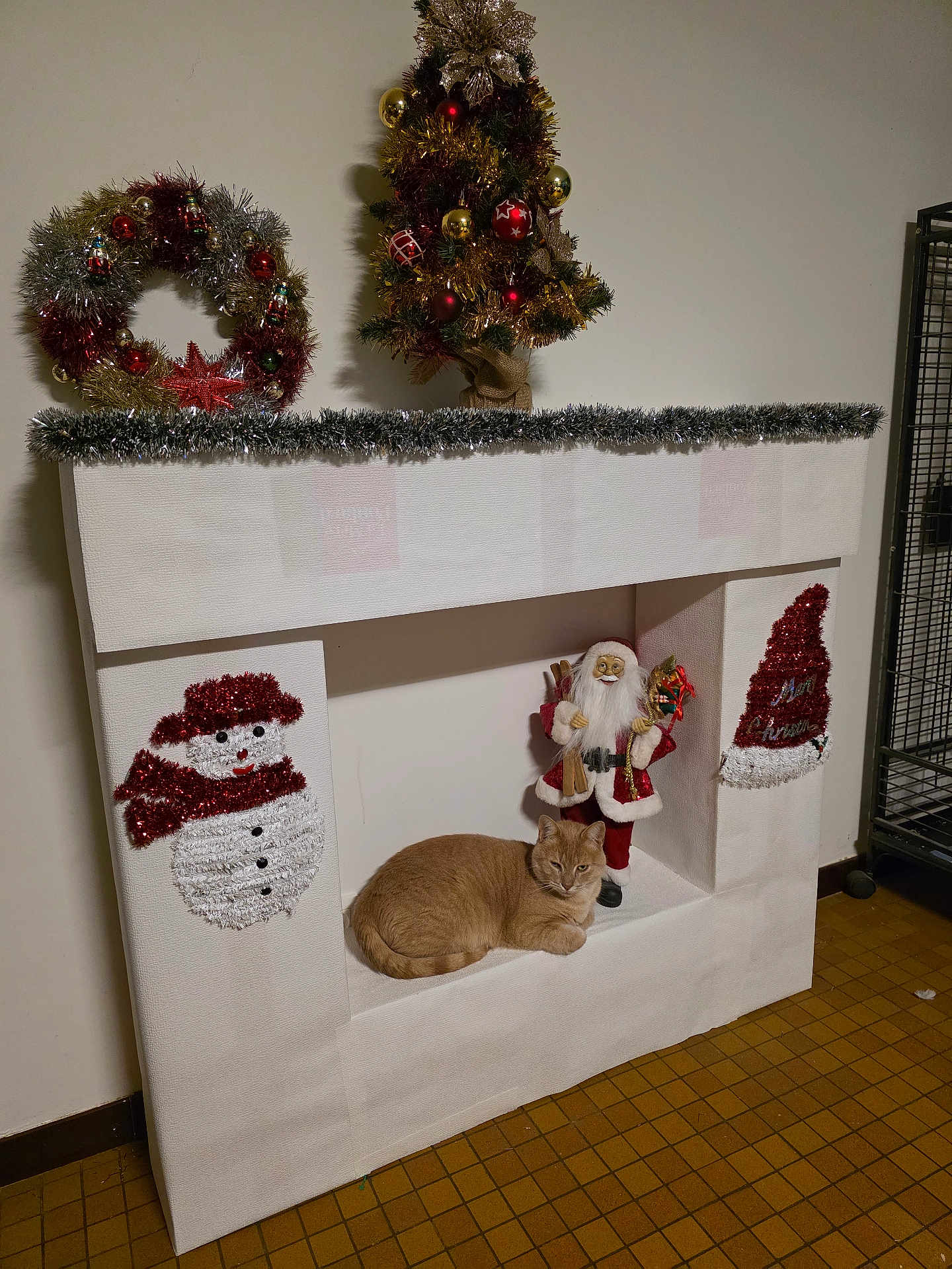 Noe a rejoint le concours — aidez-le/la à gagner de superbes lots ! cat, ginger_cat, christmas_decorations, fake_fireplace, snowman, santa_claus, christmas_tree, holiday, festive, indoor, decor, tinsel, wreath, floor, wall, home, relaxing_cat, ornaments, seasonal, celebration