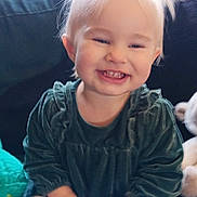 Dahlia is registered to the contest to win money with this photo: toddler, child, smiling, happy, indoor, sitting, pigtails, green_dress, white_tights, couch, plush_toy, cute, portrait, baby, hands, blonde_hair, young_child, cozy, fun, playful