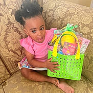 Brooklyn is registered to the contest to win money with this photo: barefoot, basket, child, clothing, colorful, couch, curly_hair, expression, furniture, girl, happy, holding, home, indoor, patterned_fabric, pink_shirt, portrait, seat, toddler, toys