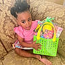 barefoot, basket, child, clothing, colorful, couch, curly_hair, expression, furniture, girl, happy, holding, home, indoor, patterned_fabric, pink_shirt, portrait, seat, toddler, toys