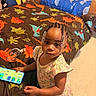 Brooklyn is registered to the contest to win money with this photo: beads, bed, blanket, braids, child, clothing, colorful, curious, dinosaur_pattern, floor, furniture, indoor, looking_up, person, playful, portrait, room, smartphone, toddler, young_child