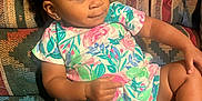 Brooklyn is registered to the contest to win money with this photo: toddler, child, girl, couch, patterned_fabric, floral_dress, pink_bow, curly_hair, indoors, sitting, barefoot, cute, young_child, relaxed, smiling, skin, legs, hand, portrait, happy