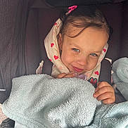 Rose a rejoint le concours — aidez-le/la à gagner de superbes lots ! toddler, child, stroller, blanket, smile, face, blue_eyes, hooded_jacket, heart_pattern, cozy, cute, portrait, baby, hand, pink_bow, clothing, young_child, indoor, candid, happy