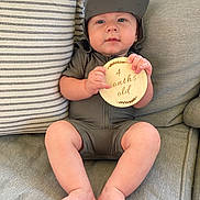 Stetson Hayes is registered to the contest to win money with this photo: baby, infant, child, couch, pillow, wooden_sign, hat, clothing, sitting, legs, feet, hands, face, expression, home, indoor, fabric, striped_pillow, cute, comfortable