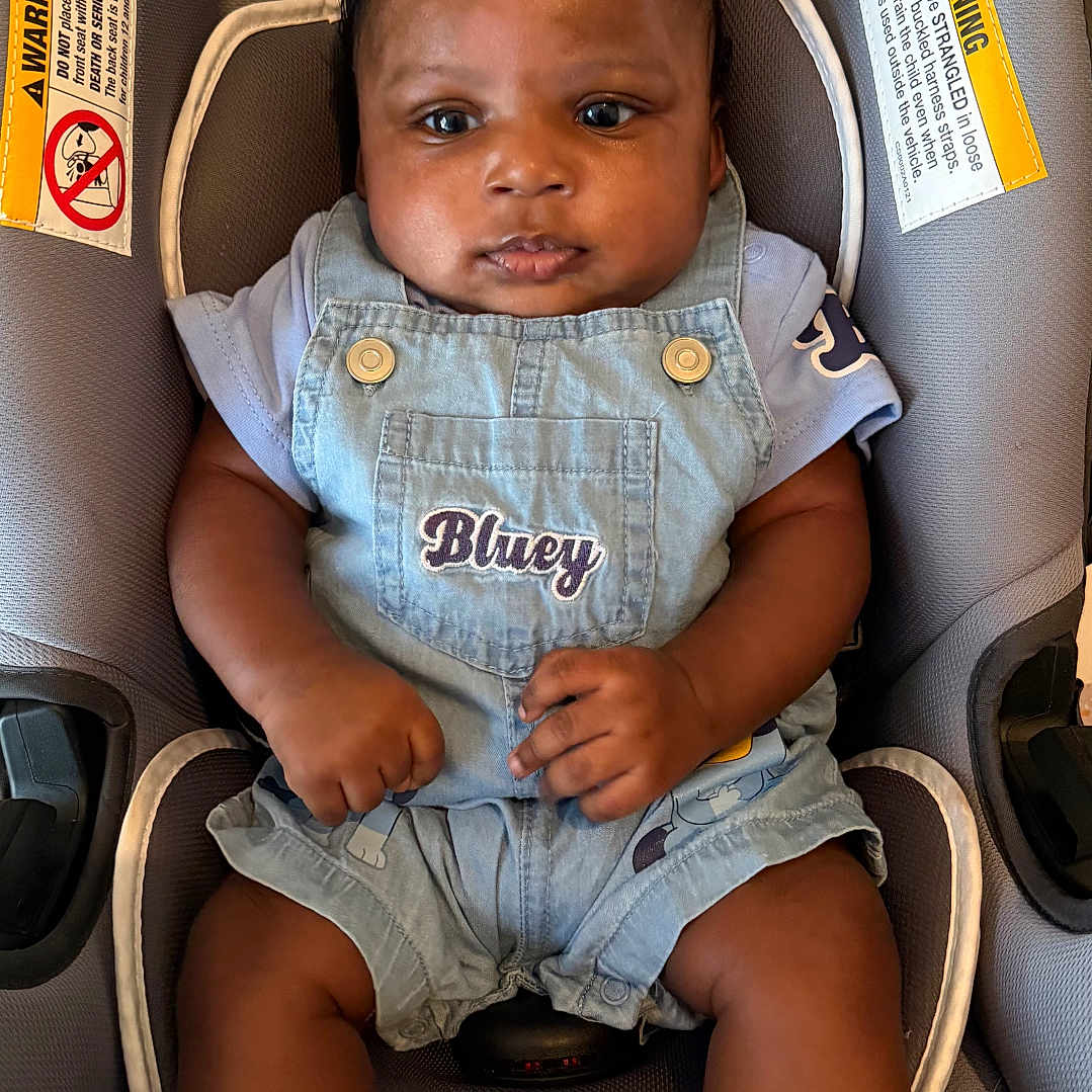 Marquiez is registered to the contest to win money with this photo: baby, child, denim_overalls, car_seat, blue_socks, infant, cute, portrait, indoor, clothing, seatbelt, comfortable, adorable, young_child, person, skin, face, hands, legs, casual_wear
