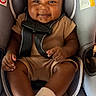 baby, child, car_seat, smiling, curly_hair, brown_outfit, white_socks, infant, seatbelt, happy, cute, indoors, portrait, young_child, sitting, person, skin, face, hands, feet