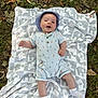 Mylo is registered to the contest to win money with this photo: baby, blanket, elephant_pattern, grass, leaves, hat, onesie, carrot_print, outdoor, infant, smiling, white_socks, nature, fall, cute, child, portrait, lying_down, soft_texture, happy