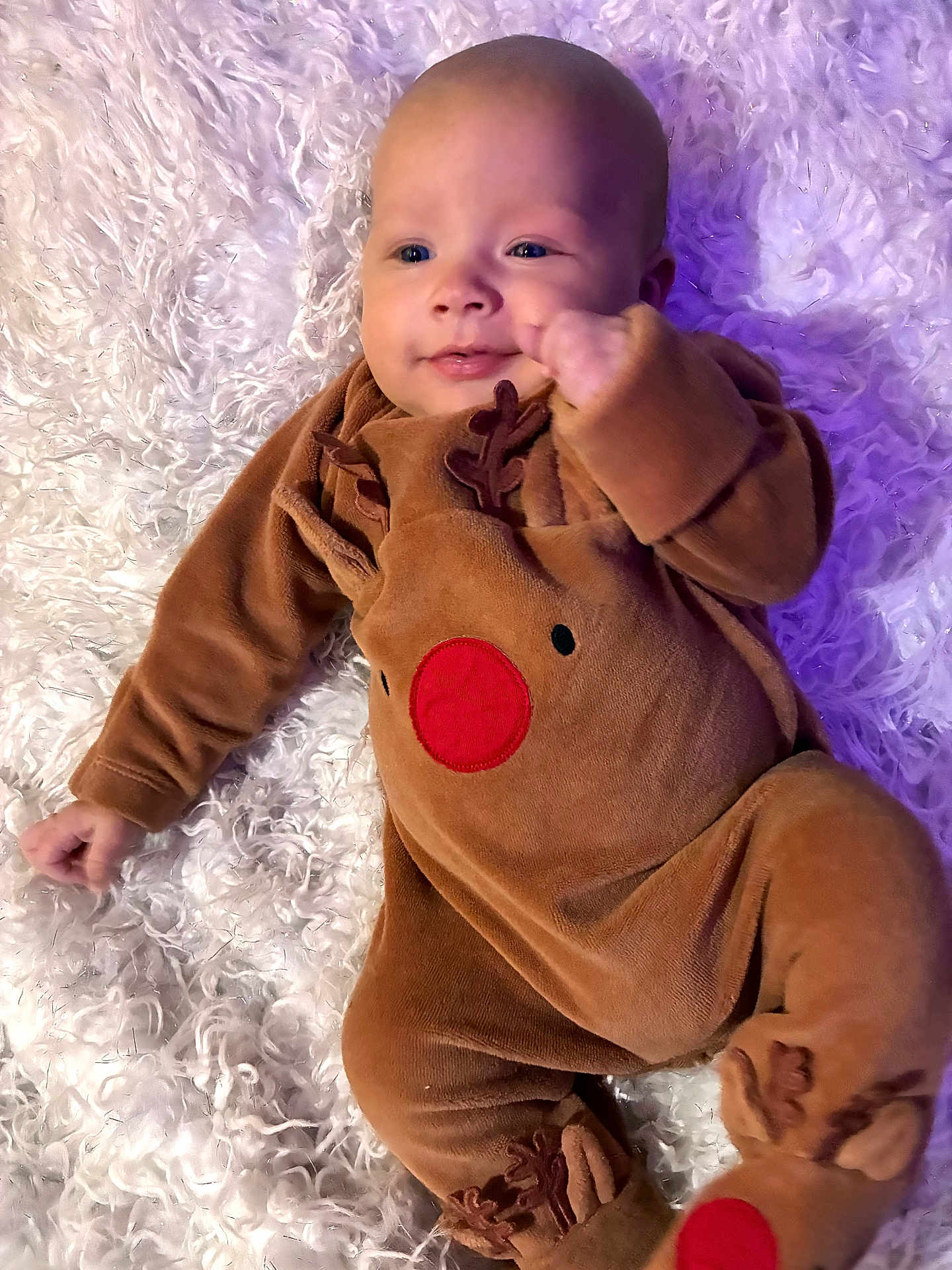 Louie joined the competition — help win amazing prizes! baby, infant, onesie, reindeer, costume, smile, face, person, child, blanket, soft_texture, cute, holiday, christmas, fur, lying_down, cozy, warm_clothing, indoors, happy