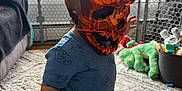 Ronan is registered to the contest to win money with this photo: toddler, child, mask, orange, skull_mask, pajamas, indoor, carpet, toy, dog, living_room, window, fan, furniture, pet, playtime, cute, home, curious, animal