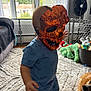 toddler, child, mask, orange, skull_mask, pajamas, indoor, carpet, toy, dog, living_room, window, fan, furniture, pet, playtime, cute, home, curious, animal