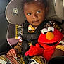 child, toddler, car_seat, seat_belt, plush_toy, elmo, pajamas, car_interior, sunlight, cute, smiling, face, hand, clothing, toy, seat, window, safety, happy, infant