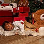 Omari is registered to the contest to win money with this photo: child, toddler, rug, teddy_bear, gift_boxes, gingerbread_plush, christmas_tree, holiday, decorations, lights, ornaments, sweater, pants, floor, couch, pillow, indoor, festive, smiling, cozy
