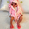 baby, child, pink_robe, pink_towel, sunglasses, flip_flops, bed, pillow, white_bedspread, cute, fashion, infant, relaxing, indoor, portrait, toddler, cozy, headwear, footwear, accessory