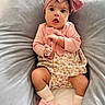 baby, child, pink_bow, headband, socks, bows, floral_dress, pink_clothing, cushion, gray_cushion, infant, cute, indoors, portrait, soft_lighting, expression, seated, baby_girl, comfort, fabric