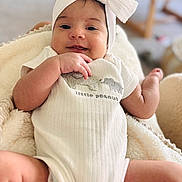 Emma joined the competition — help win amazing prizes! baby, infant, headband, bow, onesie, clothing, blanket, smile, face, hand, arm, leg, skin, indoors, soft_texture, blurred_background, cute, happy, child, person