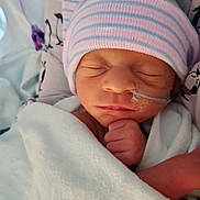 Aliyah is registered to the contest to win money with this photo: newborn, baby, sleeping, blanket, hat, striped, medical_tube, hospital, infant, hand, face, closeup, cozy, patterned_fabric, wrapped, peaceful, cute, child, person, indoors