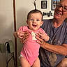 baby, casual_clothing, chair, child, door, face, family_photos, furniture, glasses, hair_ponytail, hand_holding, happy, indoor, person, pink_onesie, portrait, skin, smile, wall_decor, woman