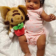 Vylen joined the competition — help win amazing prizes! baby, infant, headband, plush_toy, cat_toy, strawberry, blanket, pink_clothing, smiling, lying_down, cute, soft_texture, child, indoors, relaxed, happy, small_foot, dark_hair, toy, comfort