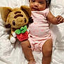baby, infant, headband, plush_toy, cat_toy, strawberry, blanket, pink_clothing, smiling, lying_down, cute, soft_texture, child, indoors, relaxed, happy, small_foot, dark_hair, toy, comfort