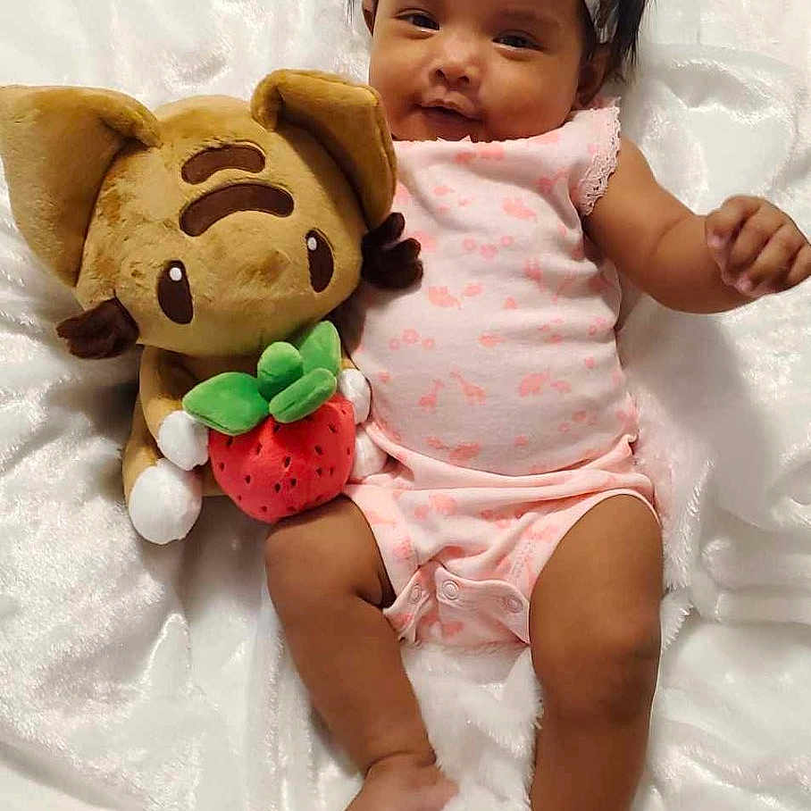 Vylen joined the competition — help win amazing prizes! baby, blanket, cat_toy, child, comfort, cute, dark_hair, happy, headband, indoors, infant, lying_down, pink_clothing, plush_toy, relaxed, small_foot, smiling, soft_texture, strawberry, toy
