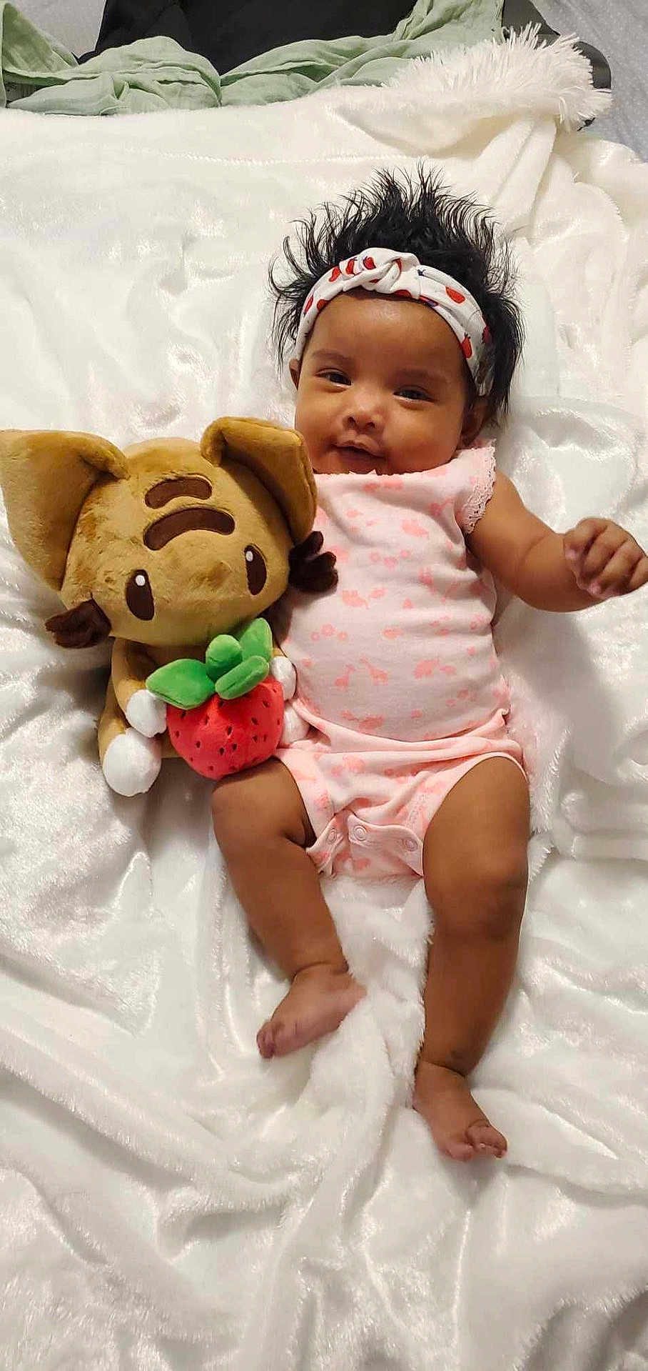 Vylen joined the competition — help win amazing prizes! baby, infant, headband, plush_toy, cat_toy, strawberry, blanket, pink_clothing, smiling, lying_down, cute, soft_texture, child, indoors, relaxed, happy, small_foot, dark_hair, toy, comfort