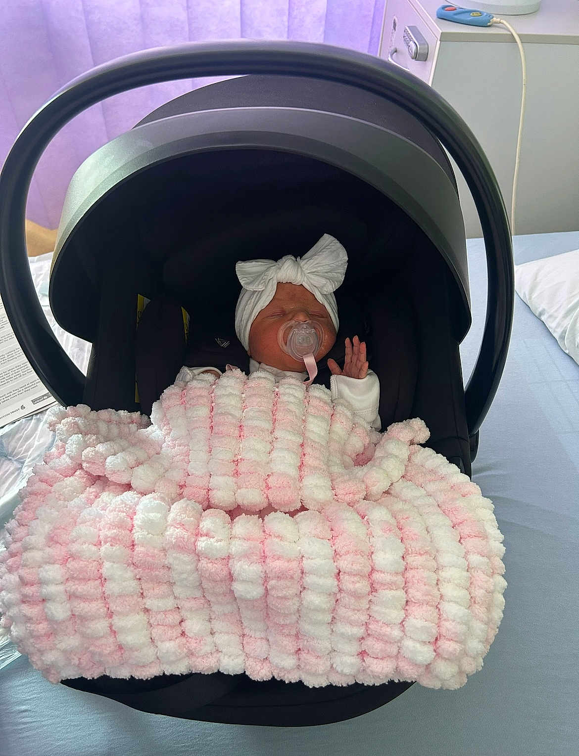 Elle joined the competition — help win amazing prizes! newborn, baby, infant_car_seat, blanket, pacifier, headband, bow, sleeping, indoors, hospital, bed, purple_curtain, soft_lighting, white_clothing, child, person, cute, resting, cozy, black_car_seat