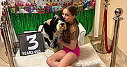 Leia joined the competition — help win amazing prizes! child, dog, birthday, indoor, balloons, sign, bench, floor, celebration, gift, banner, red_rope, stanchion, tile_floor, couch, smiling, hugging, colorful, festive, casual_clothing