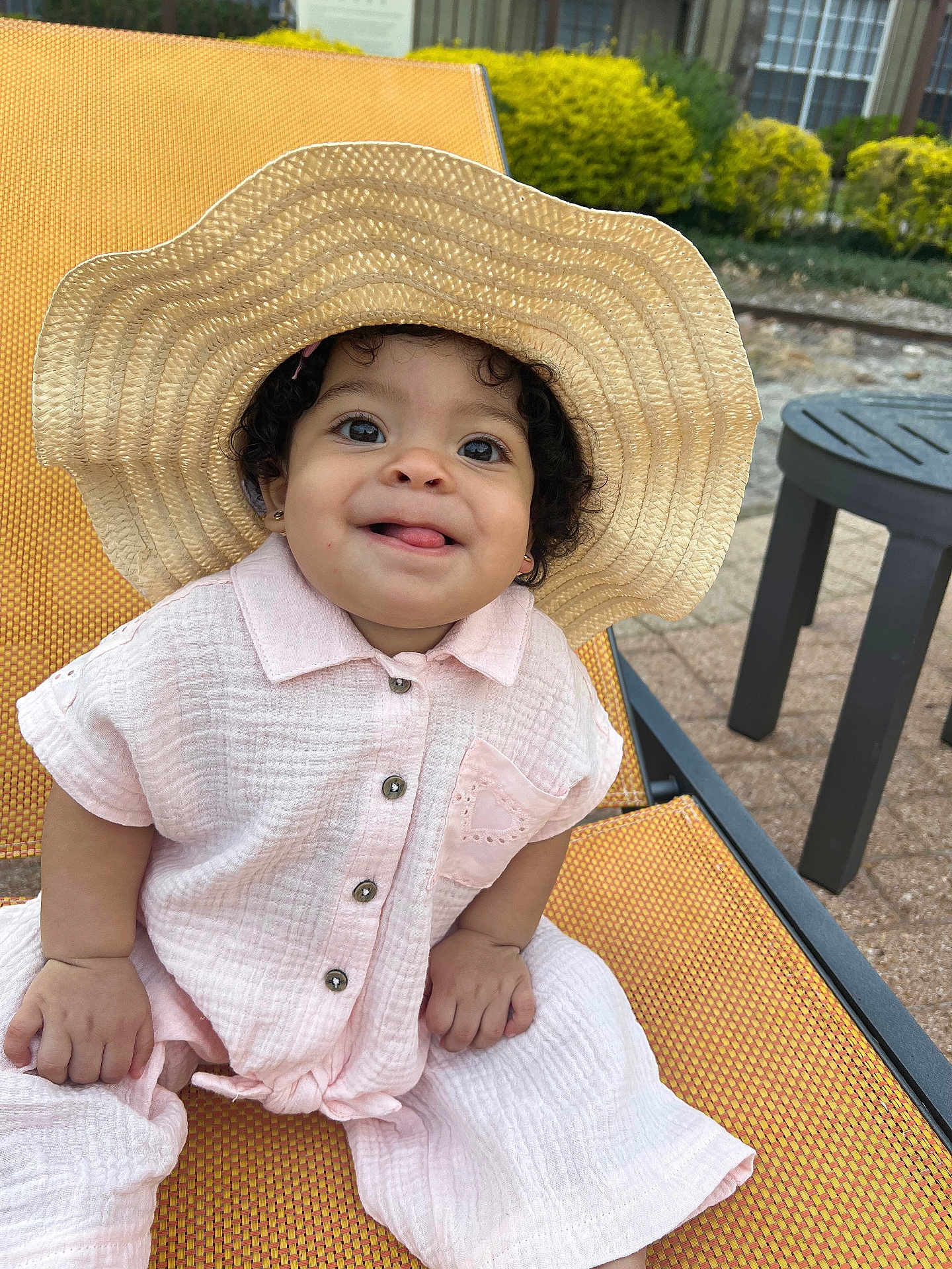 Charlotte joined the competition — help win amazing prizes! child, baby, toddler, straw_hat, hat, pink_outfit, button_shirt, smile, tongue_out, curly_hair, earrings, lounge_chair, outdoor, patio, side_table, summer, portrait, happy, hands, seat