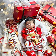 Ariana joined the competition — help win amazing prizes! baby, bokeh, candy_cane, celebration, child, christmas, cute, festive, gift_box, holiday, indoors, ornament, portrait, red_clothing, reindeer, smiling, soft_texture, star_pillow, string_lights, white_cushion