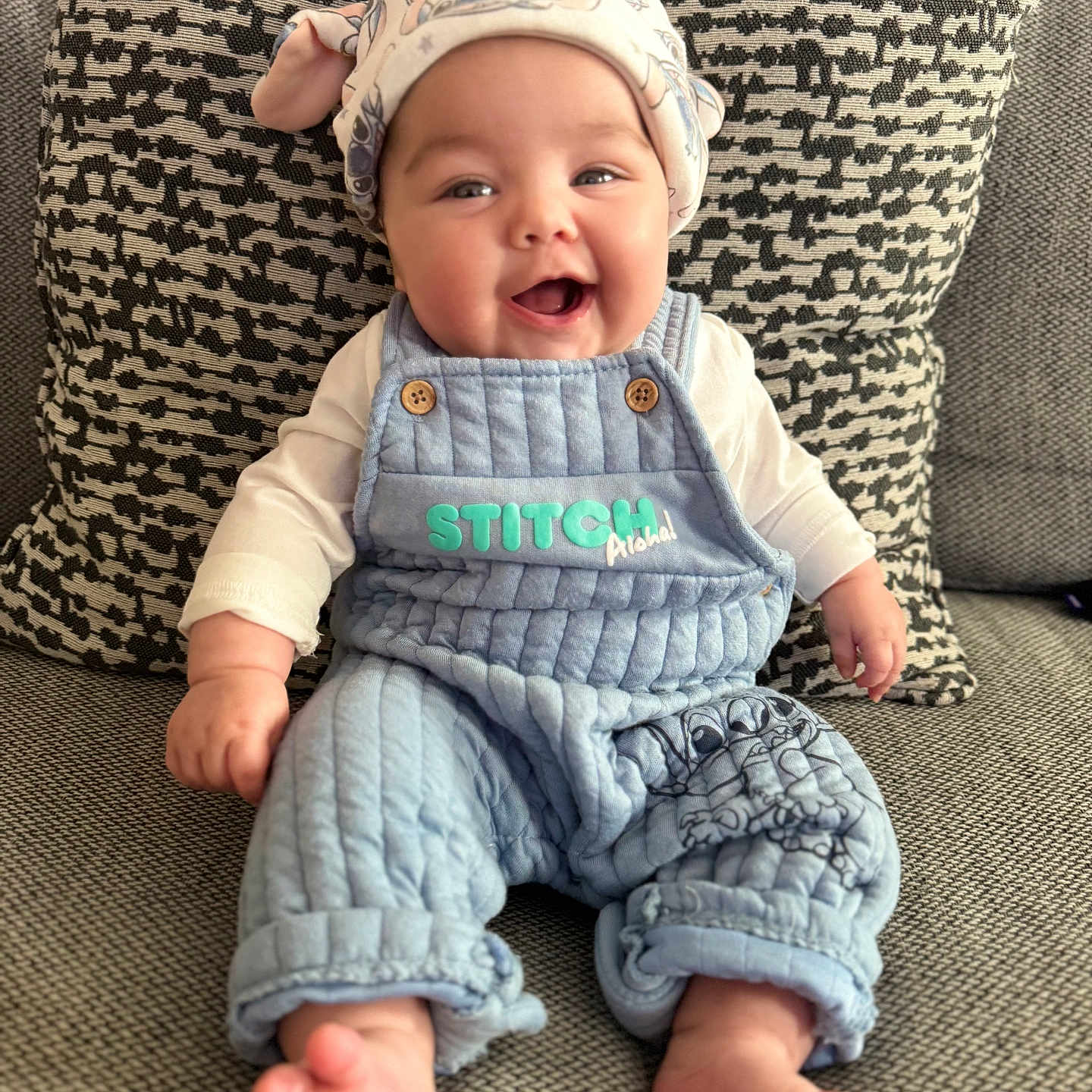 Maybel is registered to the contest to win money with this photo: baby, blue_overalls, child, clothing, comfort, couch, cozy, cute, expression, face, feet, happy, hat, indoor, infant, pillow, portrait, sitting, smiling, texture