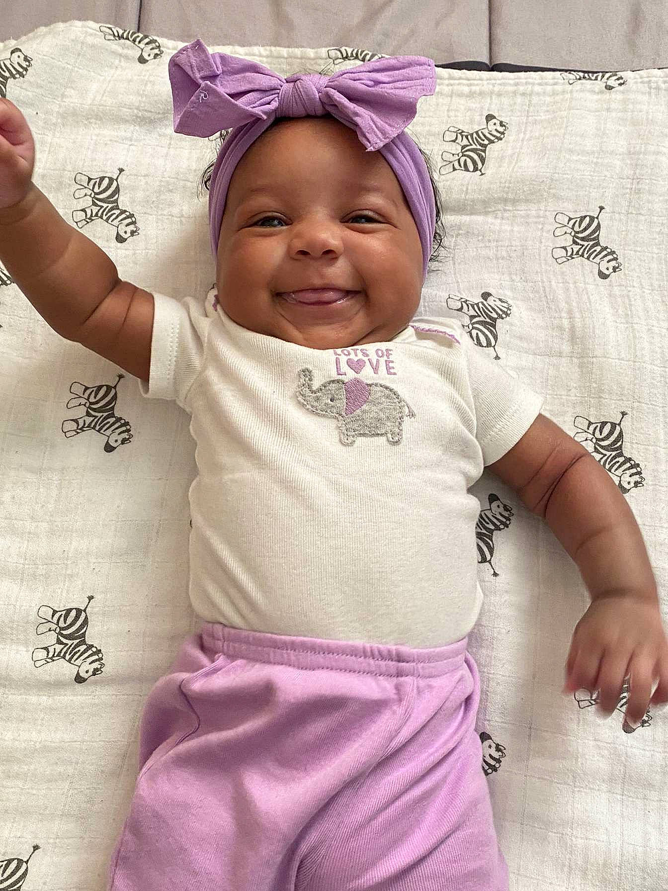 Illiana is registered to the contest to win money with this photo: baby, baby_toddler_clothing, child, gesture, happy, headwear, joy, linens, magenta, pattern, person, photograph, pink, product, purple, skin, sleeve, smile, t_shirt, textile