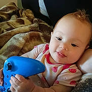 Amelia joined the competition — help win amazing prizes! baby, blanket, blue, casual, child, couch, cute, game_controller, happy, holding, human, indoor, infant, onesie, person, playing, portrait, relaxed, smiling, strawberry_pattern