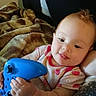 baby, blanket, blue, casual, child, couch, cute, game_controller, happy, holding, human, indoor, infant, onesie, person, playing, portrait, relaxed, smiling, strawberry_pattern