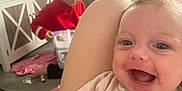 Everlie is registered to the contest to win money with this photo: baby, child, smiling, pajamas, indoor, person, furniture, cabinet, photo_frames, lamp, carpet, door, reading, book, floor, red_clothing, happy, family, home, cozy