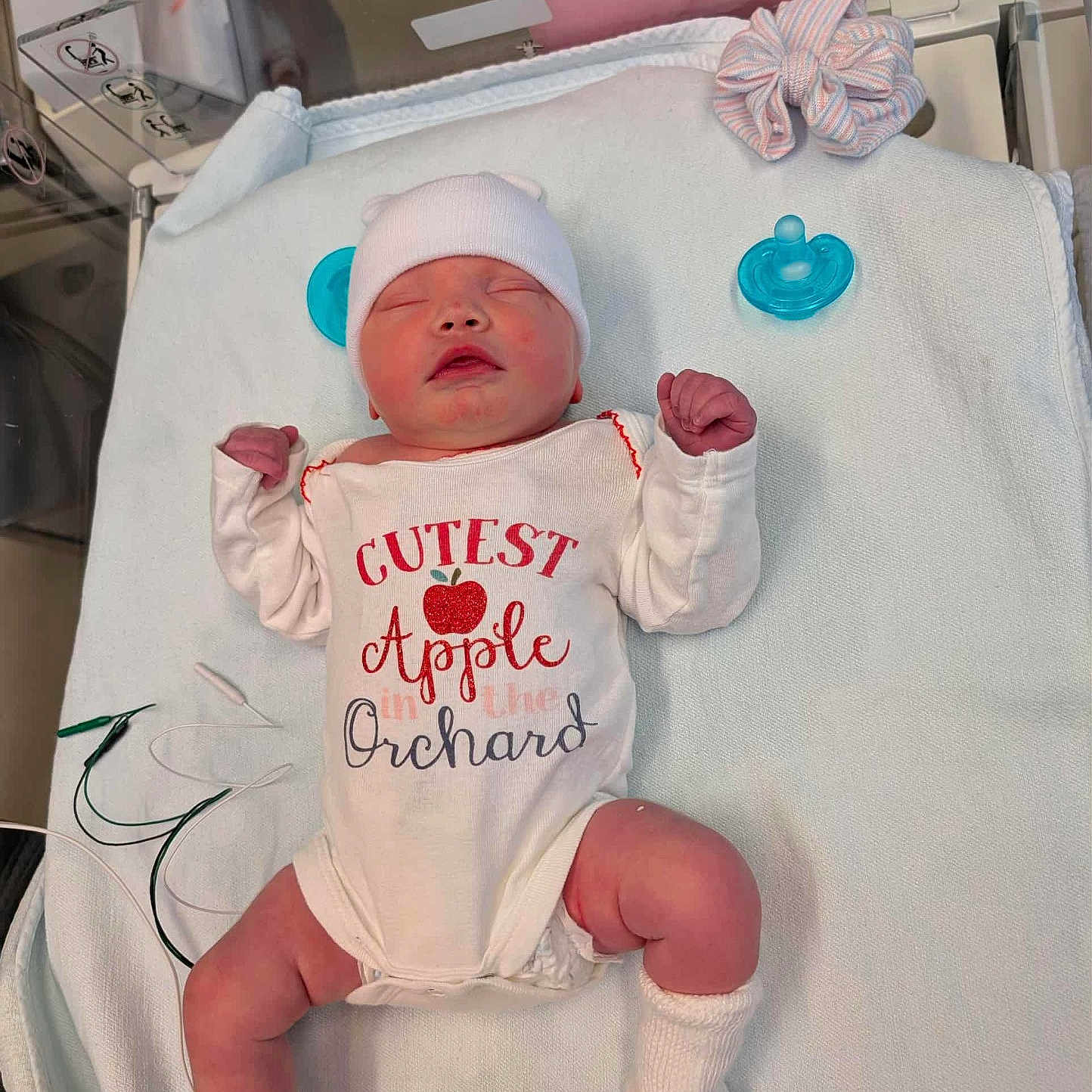 Blaire is registered to the contest to win money with this photo: baby, baby_clothes, blanket, cute, hat, hospital, infant, lying_down, medical_wires, newborn, onesie, pacifier, person, pink_skin, resting, scrunchie, sleeping, small_feet, small_hands, socks