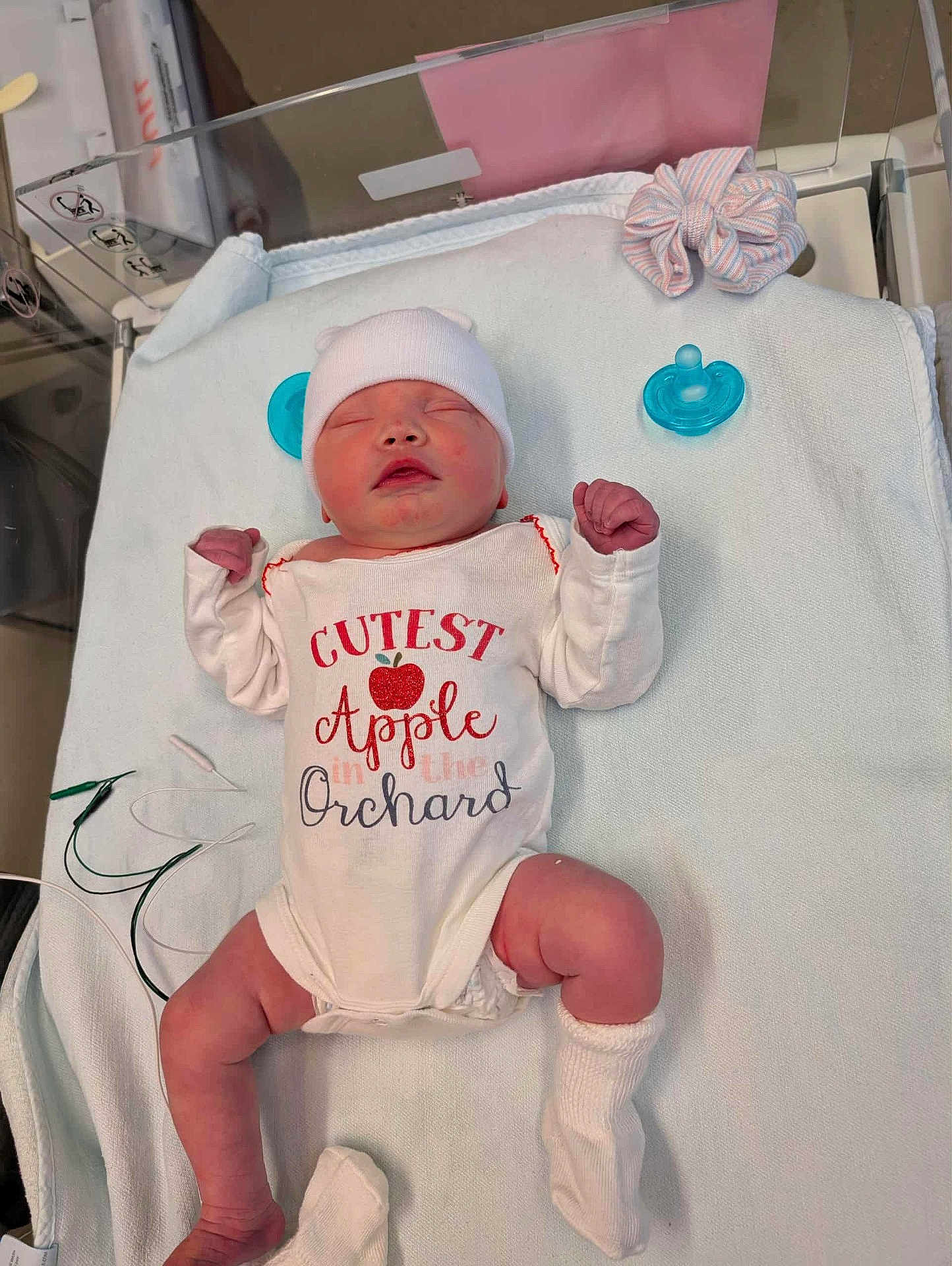 Blaire is registered to the contest to win money with this photo: newborn, baby, infant, sleeping, onesie, hat, socks, pacifier, blanket, hospital, cute, lying_down, person, baby_clothes, scrunchie, resting, small_hands, small_feet, pink_skin, medical_wires