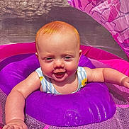 Lyra is registered to the contest to win money with this photo: baby, child, infant, red_hair, purple_inflatable, pink_mesh, sunlight, outdoor, smiling, happy, water_toy, summer, playtime, cute, young_child, baby_swim_ring, bright_colors, reaching_out, closeup, fun