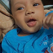 Liam joined the competition — help win amazing prizes! baby, child, face, blue_clothing, onesie, smiling, happy, infant, closeup, portrait, indoors, blanket, cute, expression, young_child, person, head, skin, hand, apparel