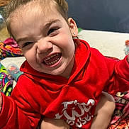 Alex joined the competition — help win amazing prizes! child, smiling, red_hoodie, indoor, blanket, happy, face, teeth, playful, person, cute, sitting, expression, earrings, legs, cozy, home, casual, portrait, fun