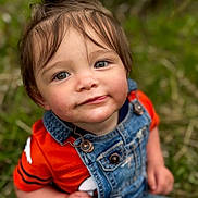 Xamiah is registered to the contest to win money with this photo: toddler, child, face, portrait, denim_overalls, orange_shirt, top_knot, grass, outdoor, nature, curious, cute, young_child, person, casual_clothing, sitting, daylight, skin, hair, eyes