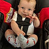 automobile, baby, black_seat, blue_eyes, car_seat, child, happy, indoors, infant, photography, portrait, red_padding, safety_harness, short_hair, sitting, smiling, striped_socks, vehicle, waving, white_shirt